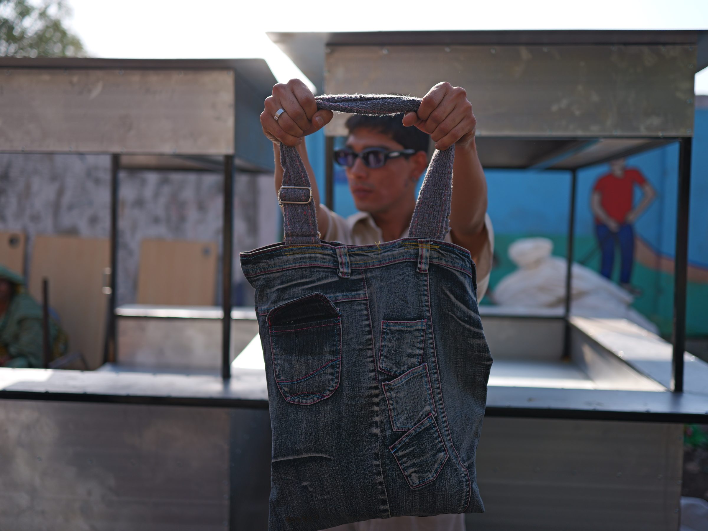 a man at a market stall holding a pocketed denim tote up toward the camera