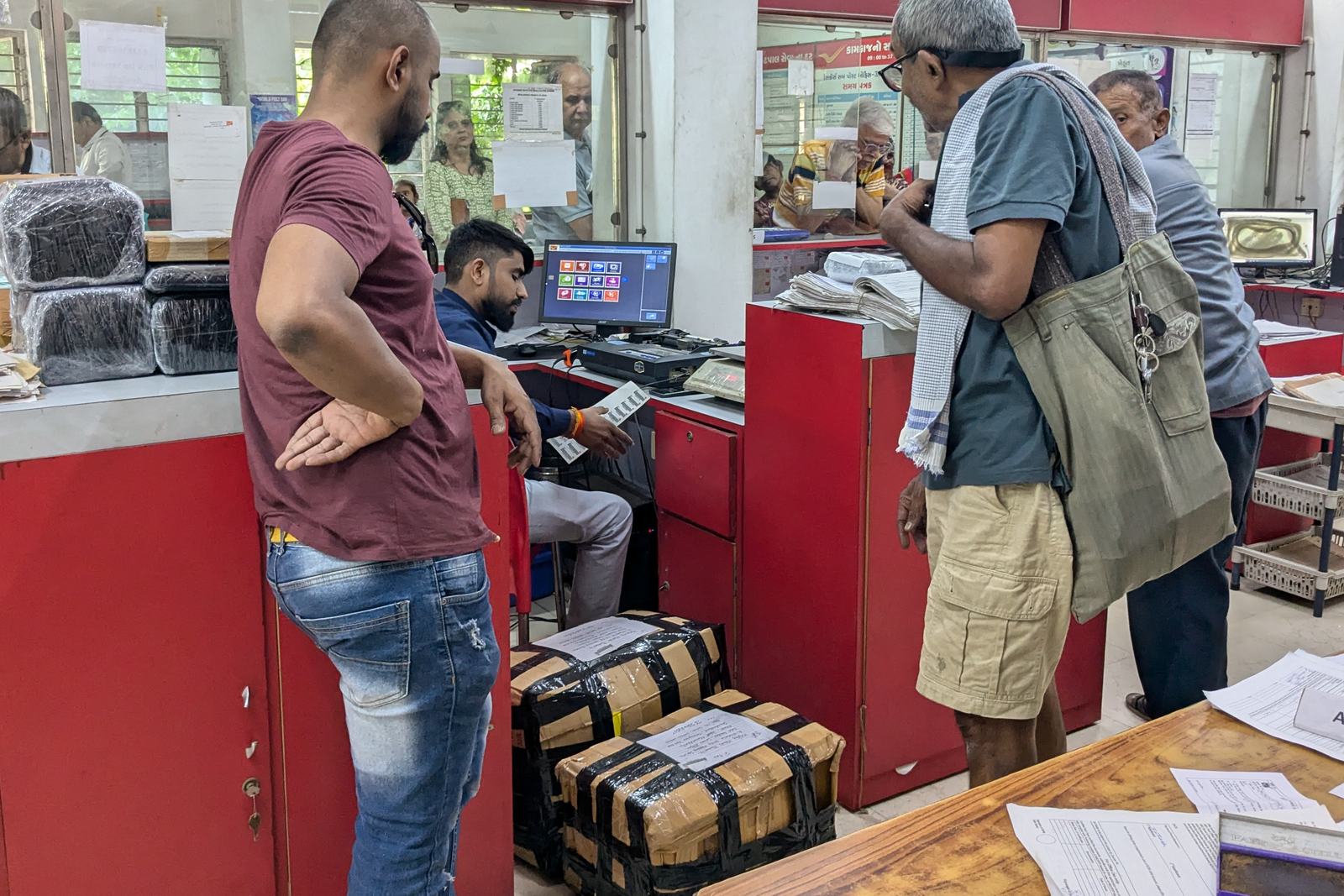 people at a post office counter, with taped parcels at their feet