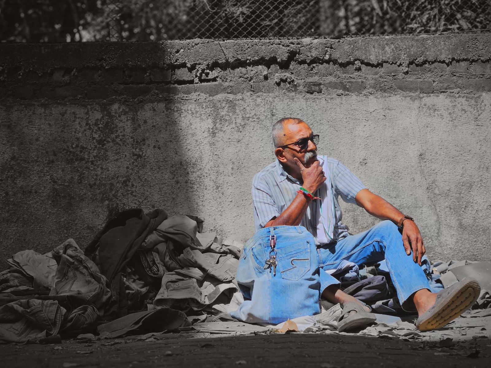 mehul sits on a heap of post-consumer denim against a concrete wall, hand on his chin