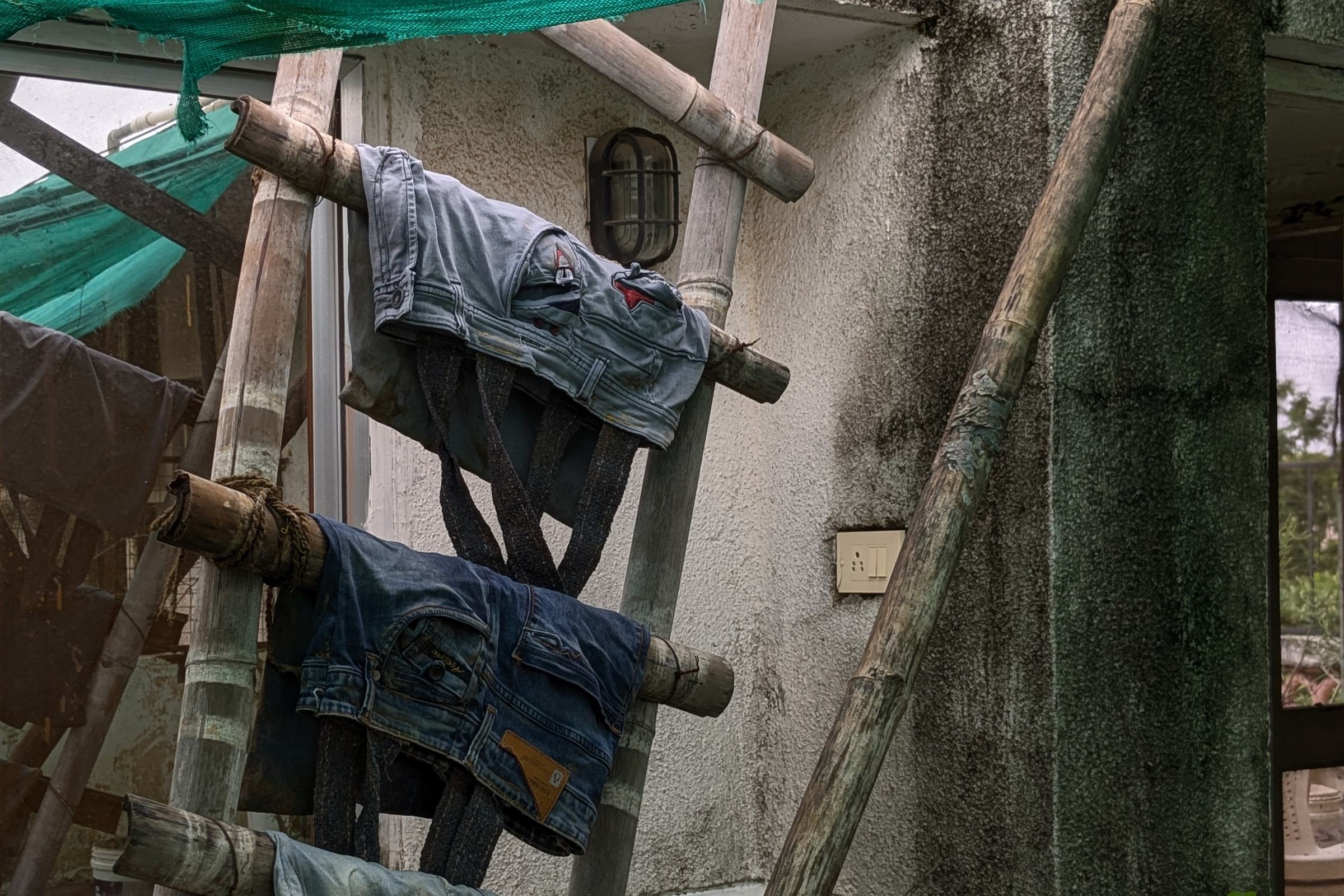 pairs of jeans hung on a bamboo ladder outdoors