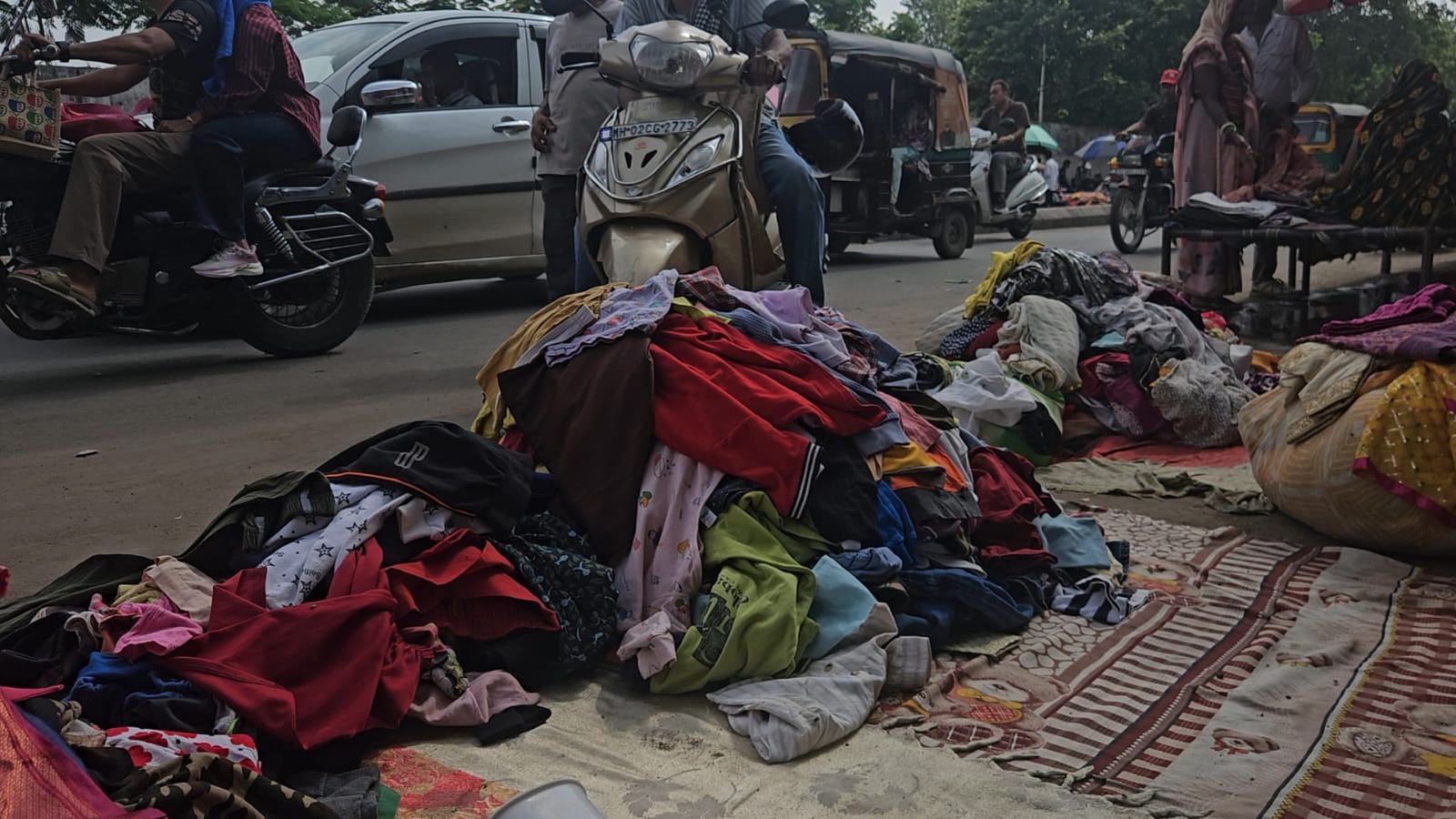 heaps of second-hand clothes laid out on cloth beside a busy road