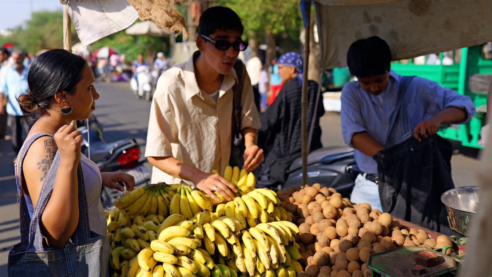 people with denim bags beside a fruit stall piled with bananas