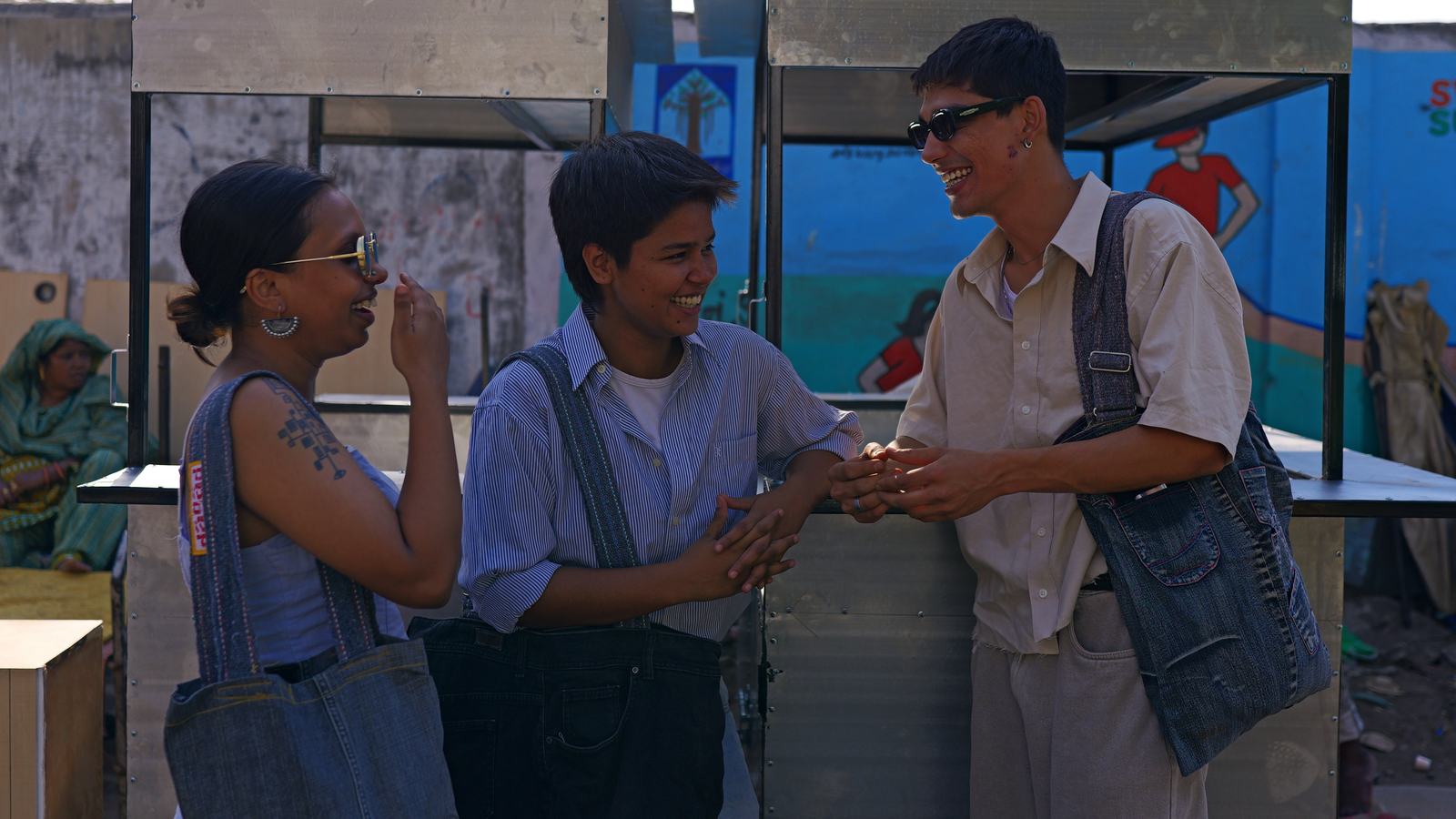 three people talking at a market stall, two with denim bags on their shoulders